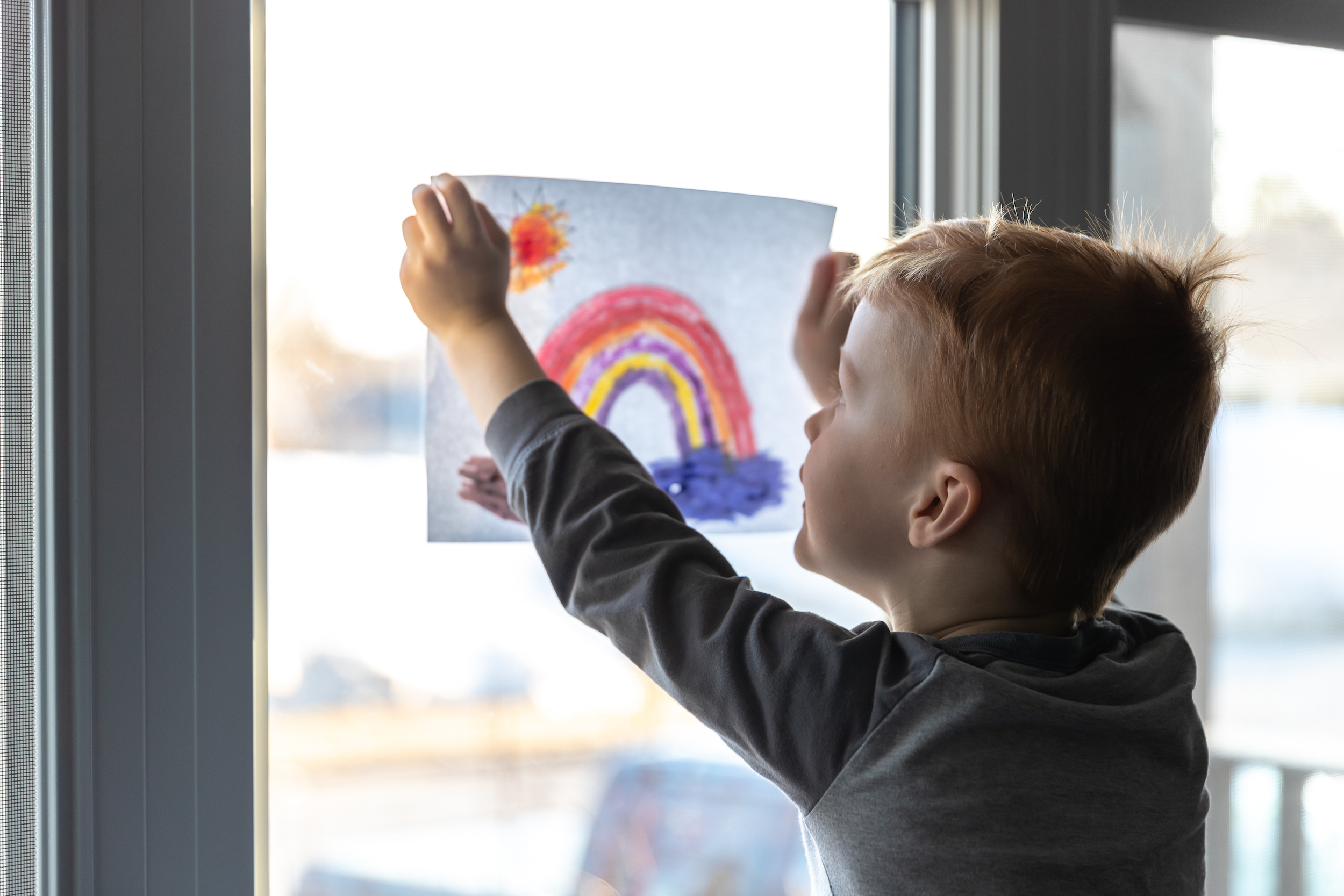 young boy sticking his drawing on home window