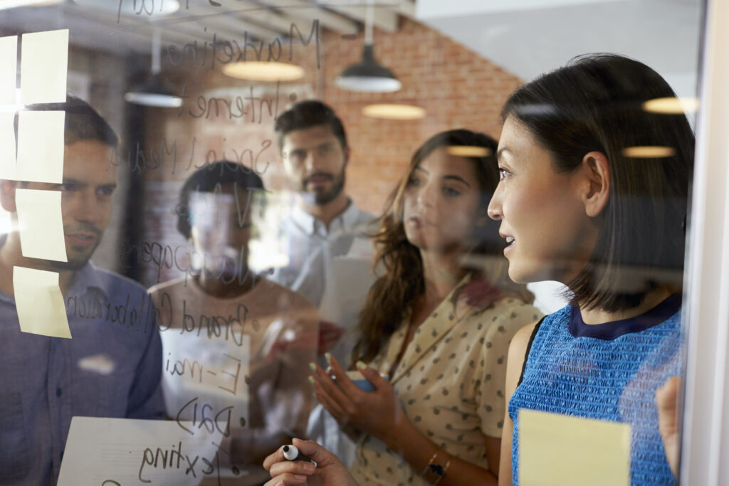 Businesswoman Writing Ideas On Glass Screen During Meeting