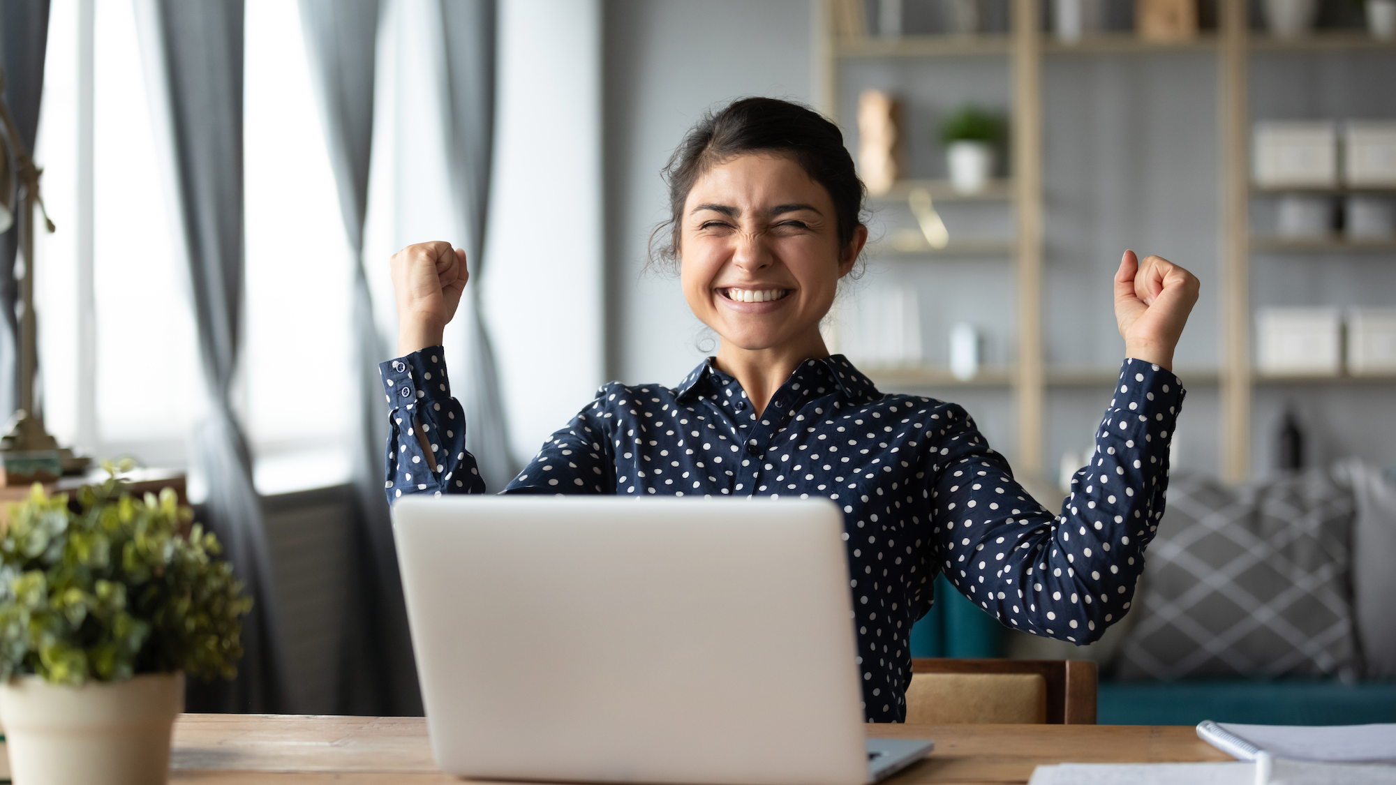 woman celebrating while looking at laptop