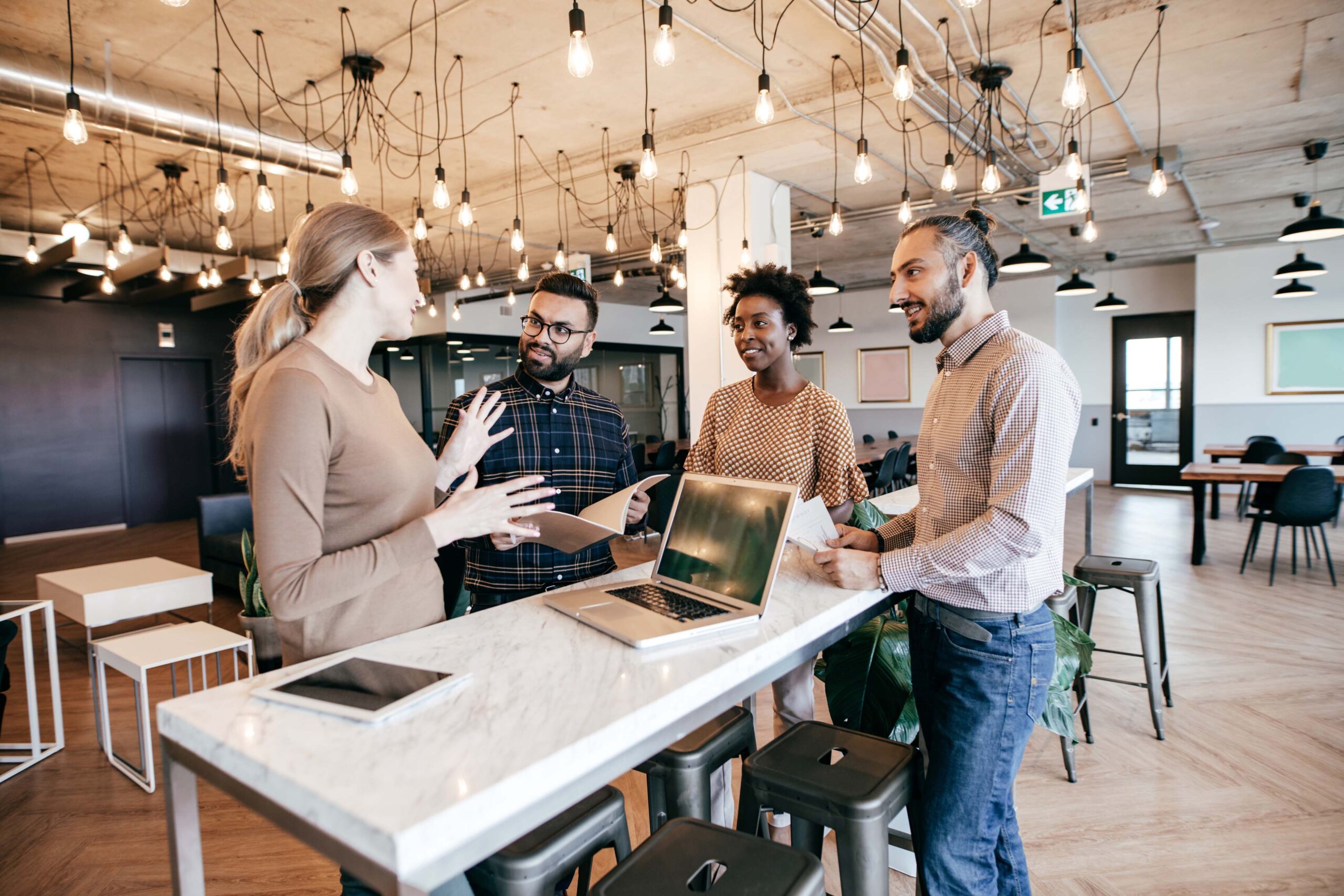 two woman talking with two men at a table with a laptop