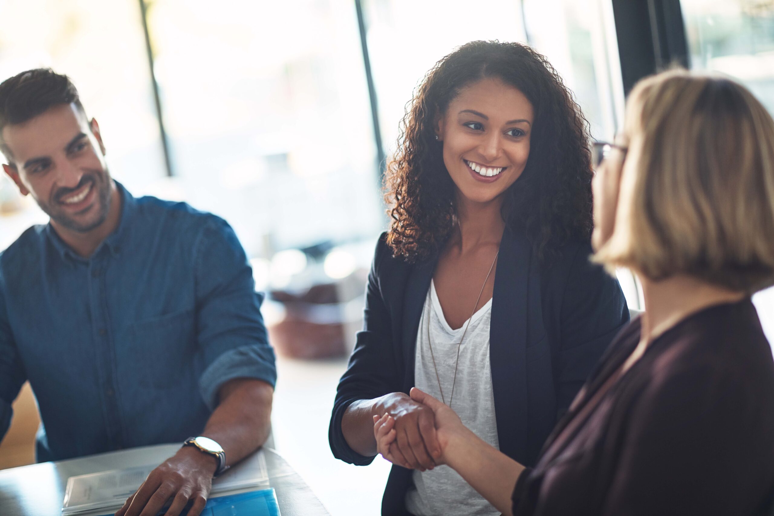 women with administrative credential smiling and shaking hands next to a smiling man