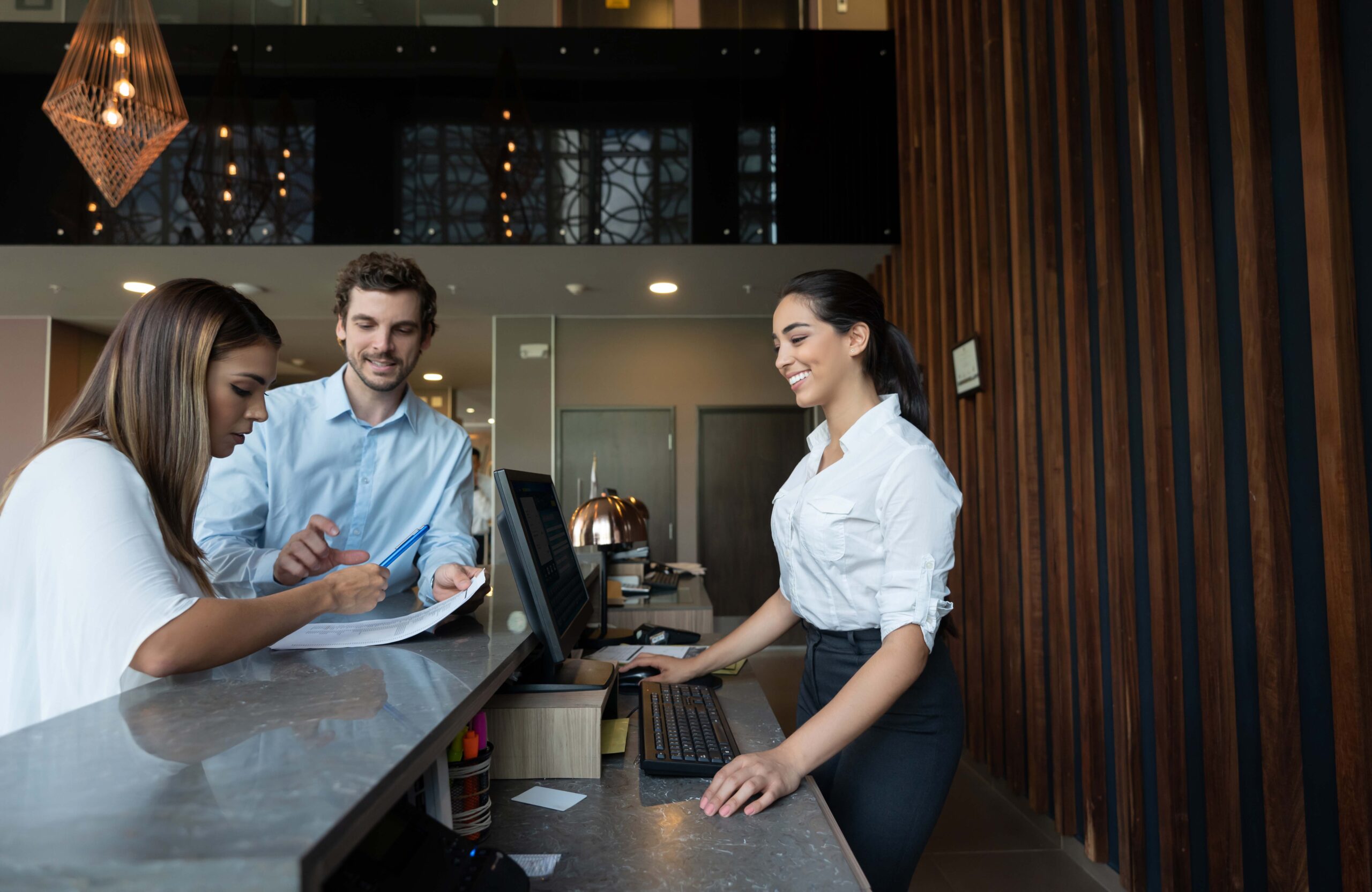 woman behind counter at a laptop attending to a man and a woman checking in