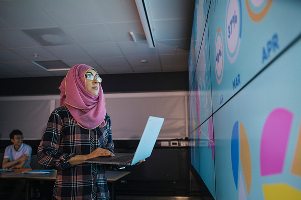 student facing large screen holding a laptop in one of the graduate programs in the Bay Area