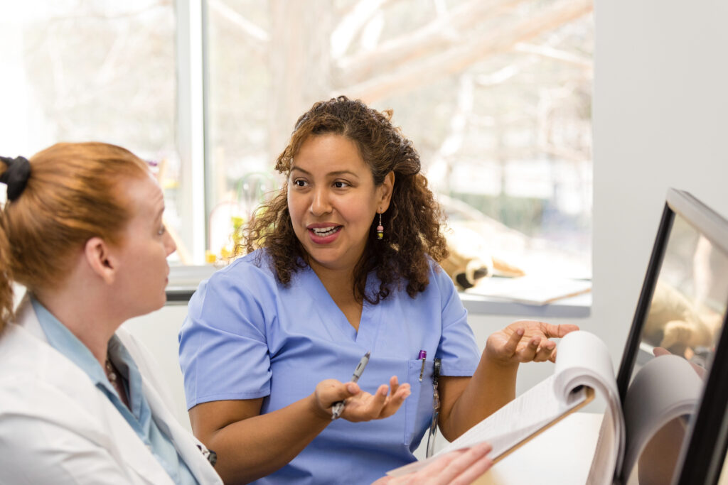 A mature adult doctor and her mid adult nurse discuss the pros and cons of various treatment options for a patient.