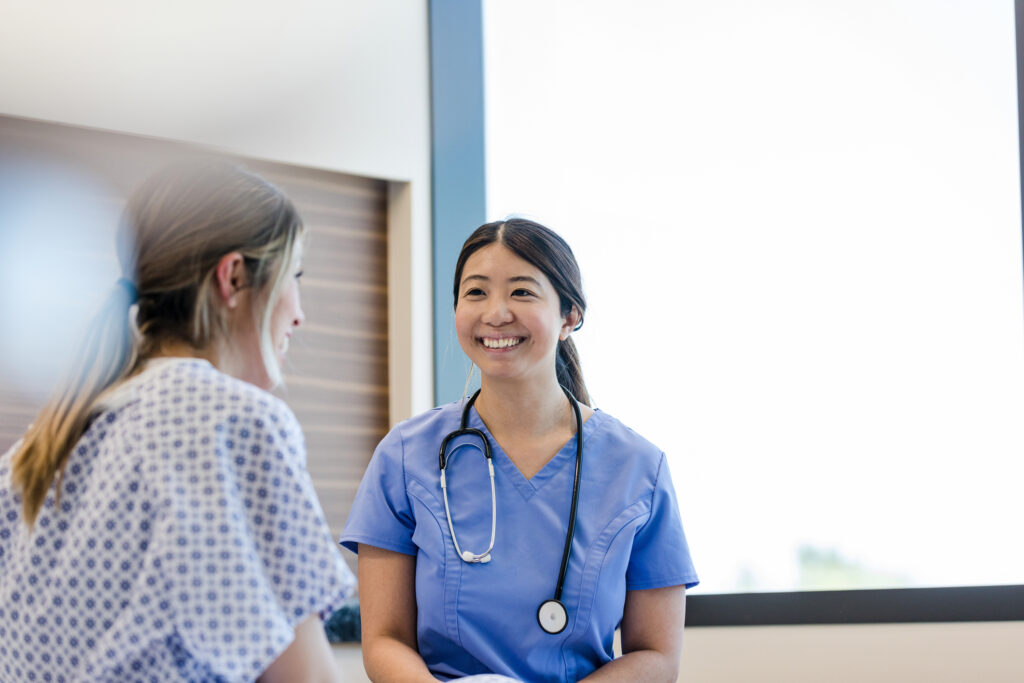A woman in blue scrubs smiling with a stethoscope around her neck