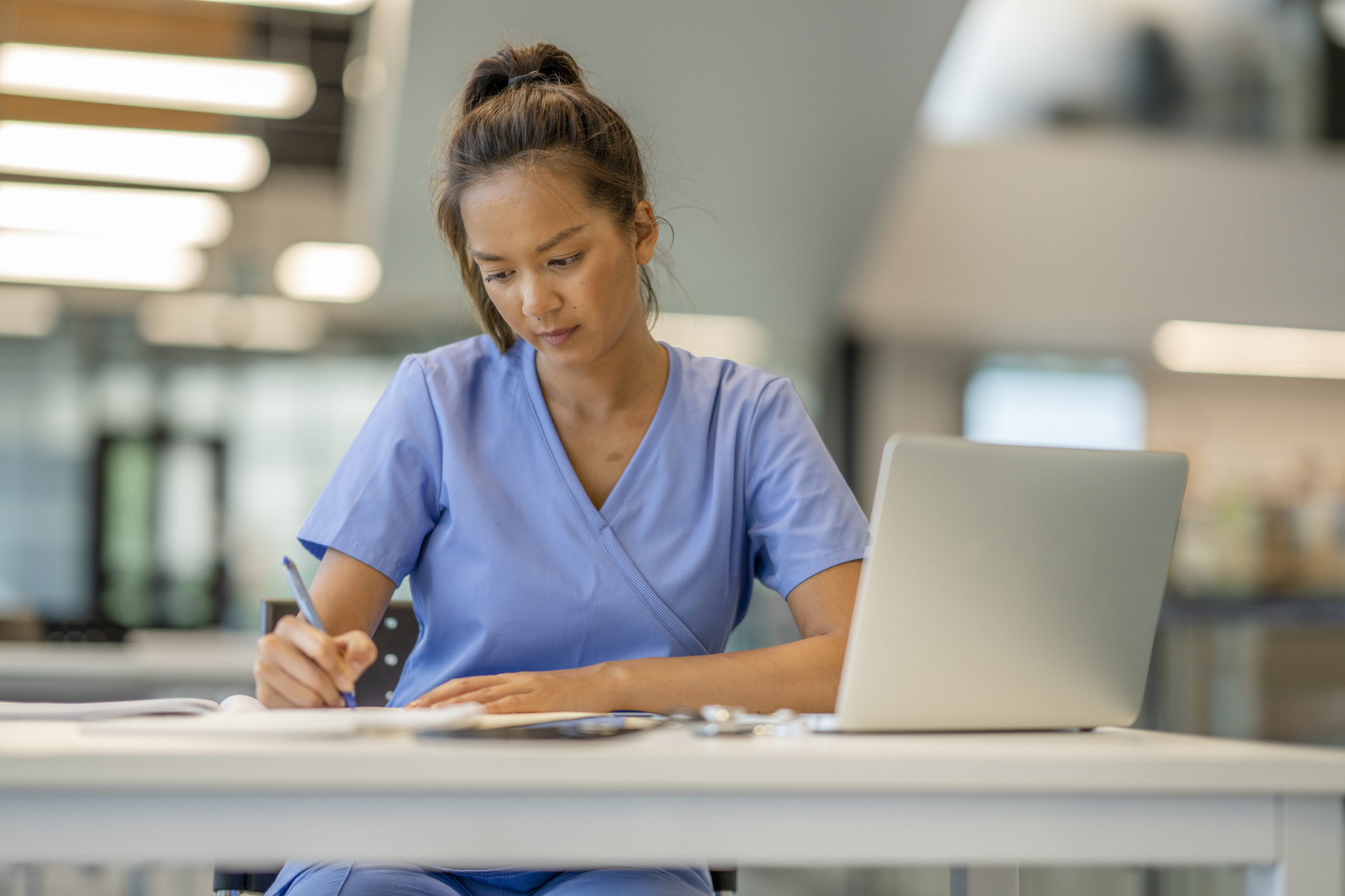 A woman in blue scrubs writing on a paper