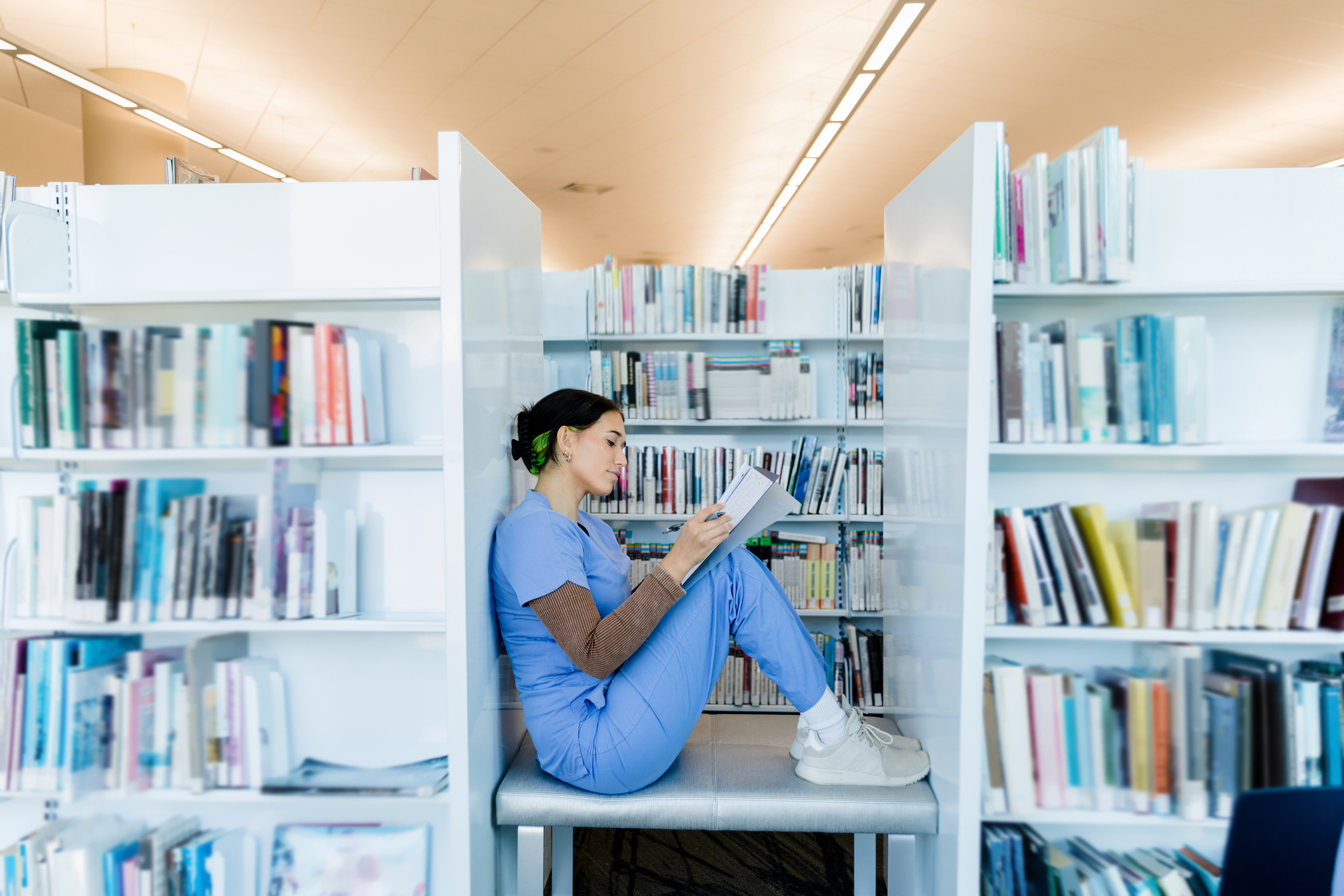 A woman sitting on a chair reading a book in a library