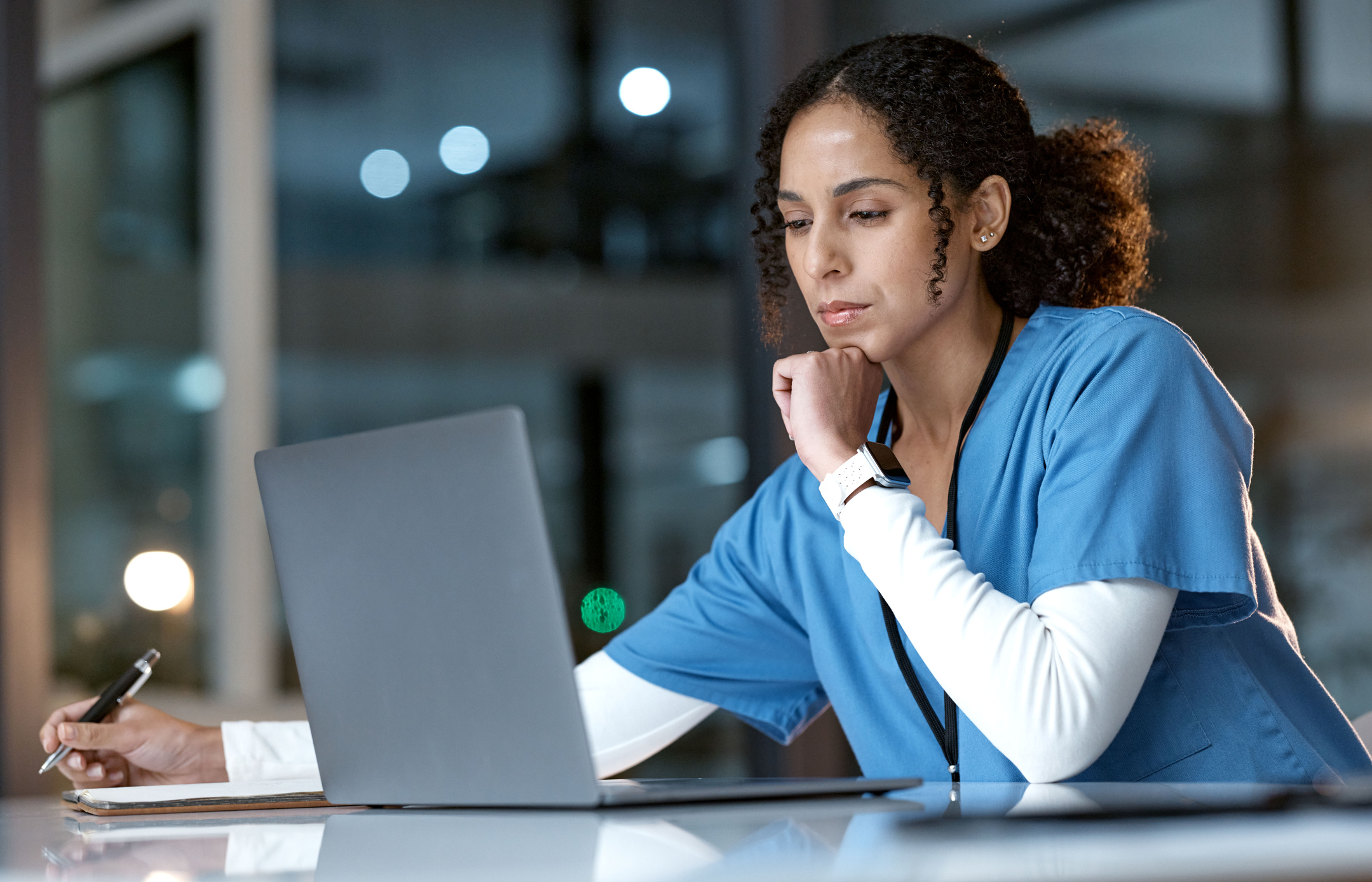 A woman in blue scrubs looking at a laptop