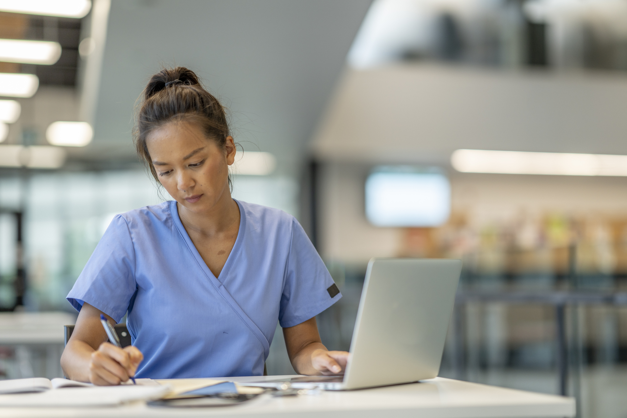 A woman in a scrubs writing on a laptop