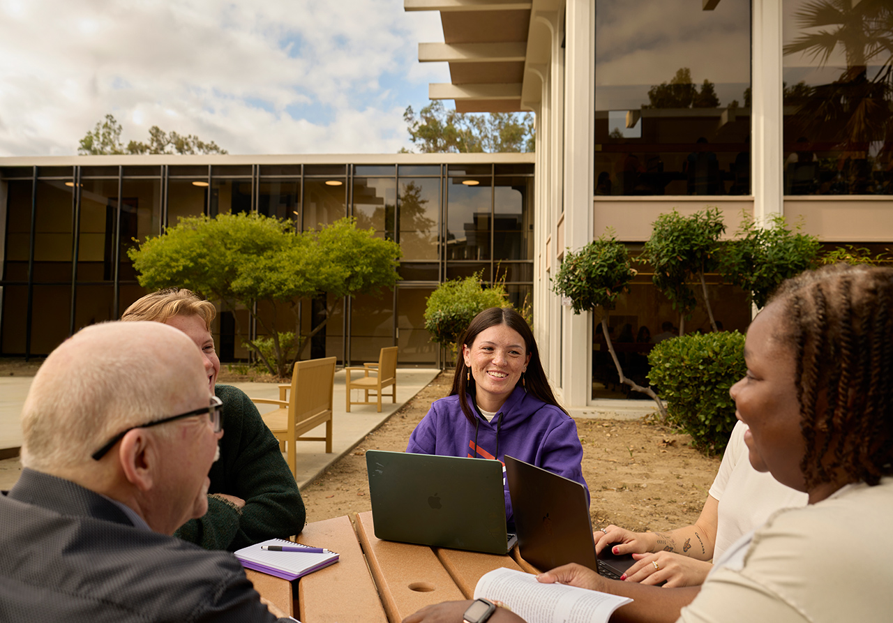 A group of people sitting around a table with laptops
