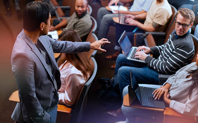 A man pointing to a man in front of a group of people using laptops