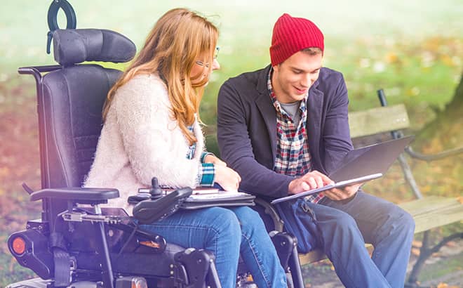 A man and woman sitting on a bench looking at a tablet